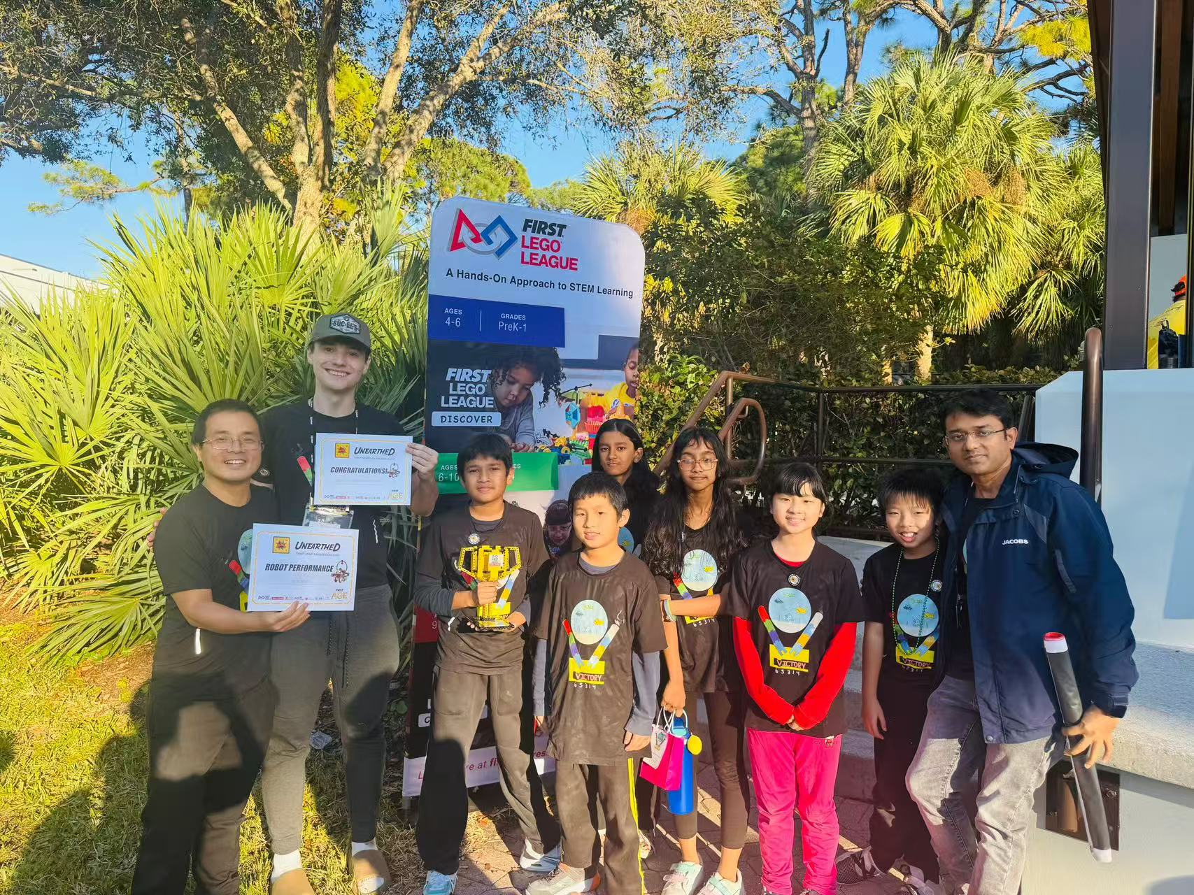 South Florida STEM Association students and mentors holding FIRST LEGO League awards and certificates outdoors