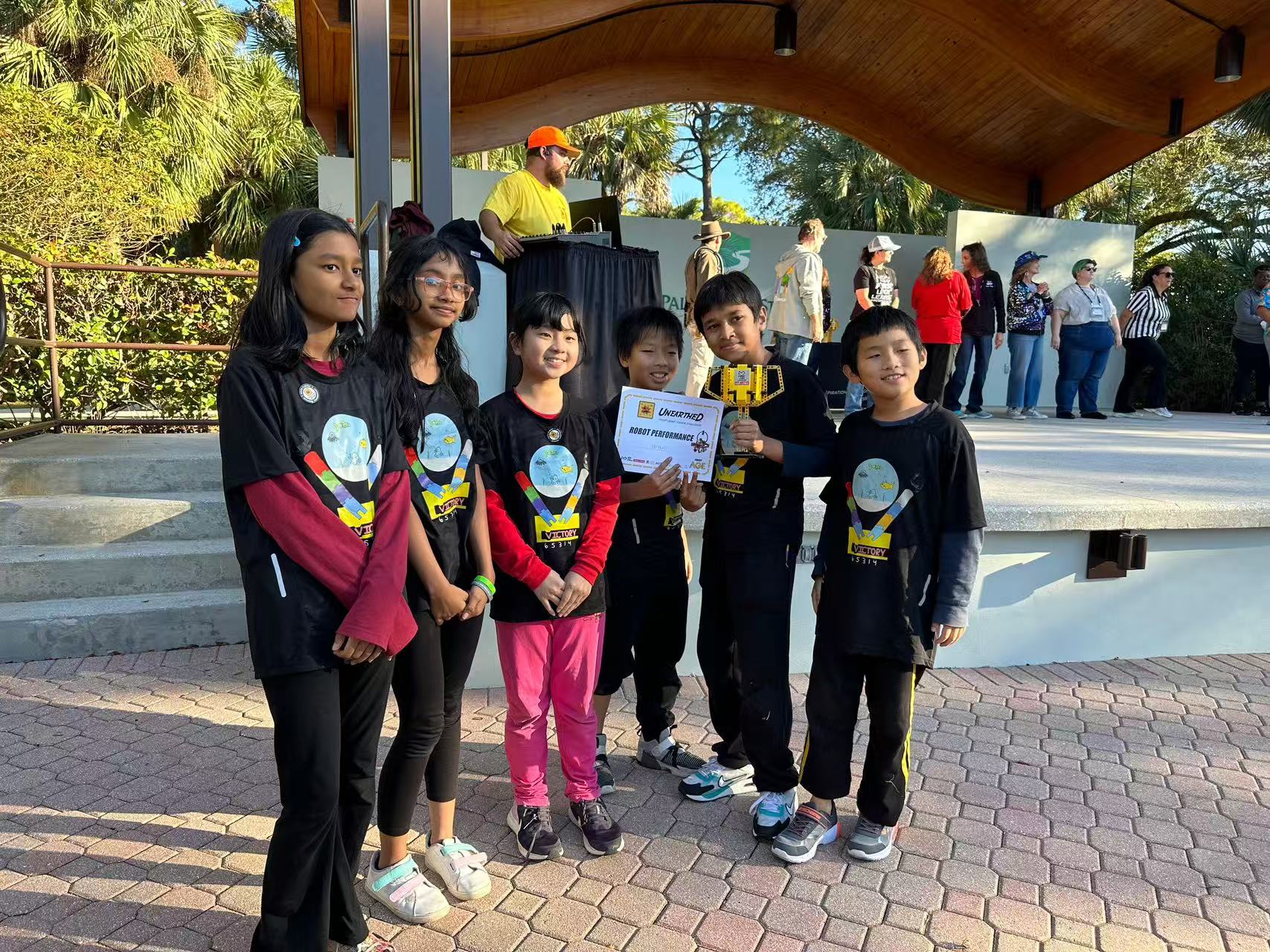 Students holding a certificate under an outdoor pavilion